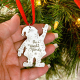 Hand holding a Santa shaped Christmas ornament with custom family text against a festive background.