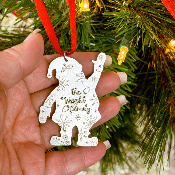 Hand holding a Santa shaped Christmas ornament with custom family text against a festive background.
