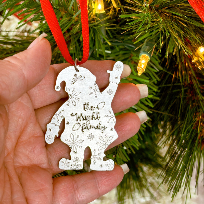 Hand holding a Santa shaped Christmas ornament with custom family text against a festive background.