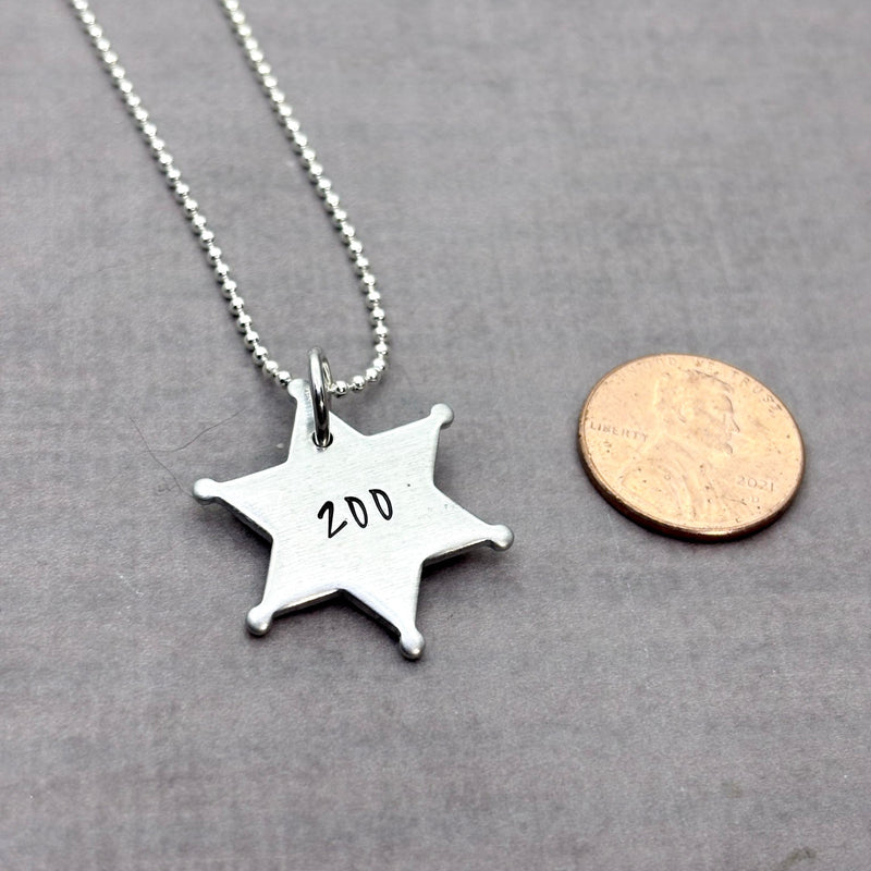 Star badge for Sheriff set next to a penny to show size.