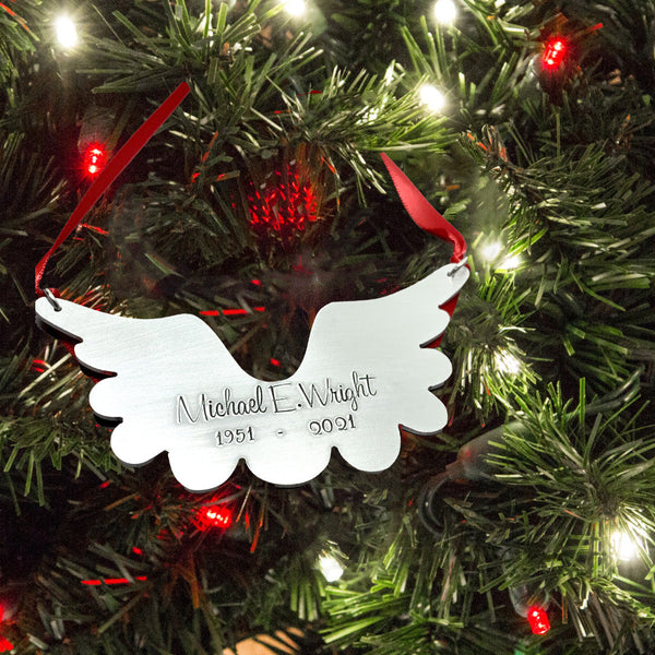 Silver angel wing ornament with engraved text on a Christmas tree.