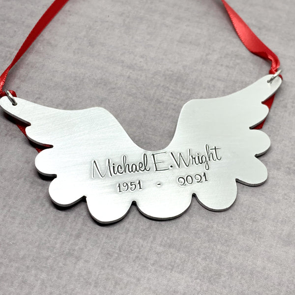 Metallic angel wing ornament with engraved text on a gray background