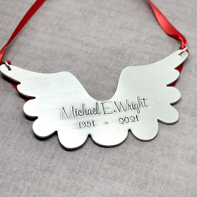 Metallic angel wing ornament with engraved text on a gray background
